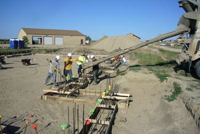 Local crew pouring concrete into wooden forms for a new commercial building footing