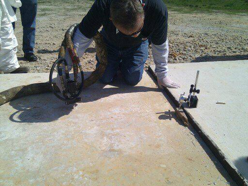 Local technician injecting expanding polyurethane foam beneath a sunken concrete slab to raise and level it