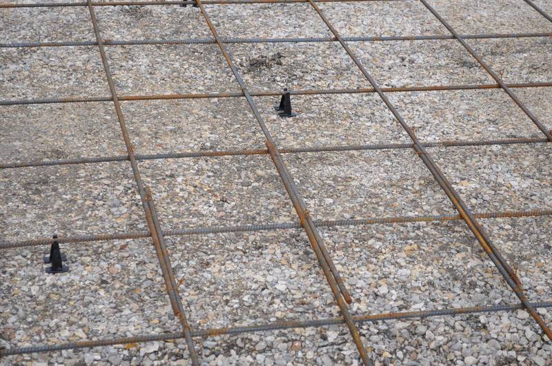 Steel rebar reinforcement grid tied on chairs over a compacted gravel base before a concrete driveway pour